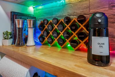 Your fully equipped kitchen features a creative spice rack with colorful ambient lighting, plus olive oil and coffee dispensers for gourmet cooking adventures.