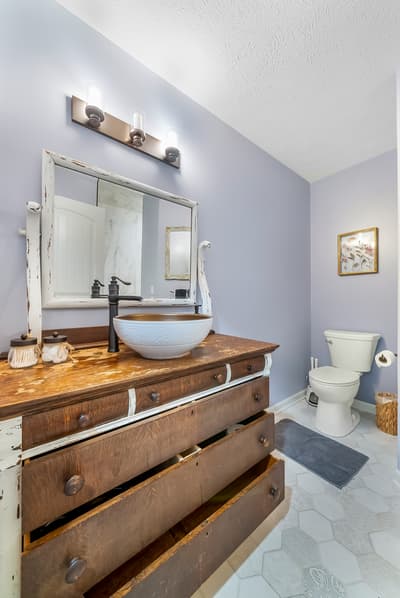 Unwind in this charming rustic bathroom featuring a unique vessel sink atop vintage drawers, creating your own spa-like retreat.