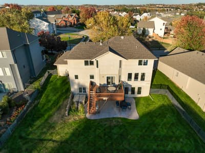 Aerial view of modern two-story home with spacious deck and patio in quiet residential neighborhood surrounded by autumn foliage.