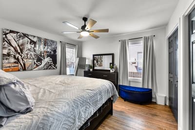 Drift into comfort beneath the gentle ceiling fan in your stylish bedroom, where art-filled walls and warm hardwood floors create the perfect retreat.