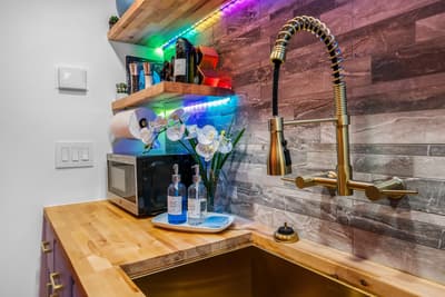 Your stylish kitchen features warm wood countertops, brass fixtures, and vibrant LED lighting that creates the perfect ambiance for preparing meals.