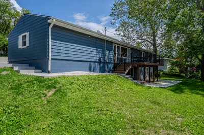 Blue siding ranch-style home nestled among mature trees with spacious lawn and elevated deck overlooking peaceful residential neighborhood.