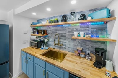 Your stylish kitchen features vibrant blue cabinets, warm wood countertops, and colorful LED-lit shelving for easy meal prep.