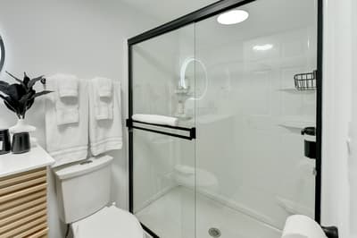 Step into your sleek modern bathroom featuring a spacious glass shower, fluffy white towels, and thoughtful touches like fresh greenery.