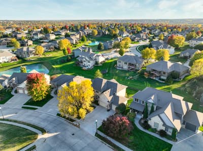 Aerial view of an established residential neighborhood featuring well-maintained homes, mature trees displaying vibrant autumn foliage, manicured lawns, and quiet suburban streets.