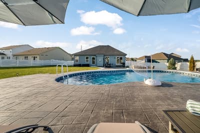 Sparkling pool awaits with comfortable deck lounging and peaceful suburban setting.