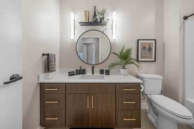 Your modern bathroom features a sleek vanity with gold accents, perfect lighting for your morning routine, and thoughtful touches like fresh greenery.