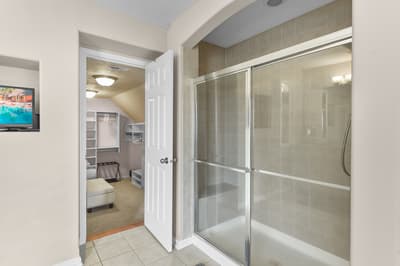 Step into your spacious bathroom featuring a gleaming glass shower and glimpse the organized bedroom beyond.
