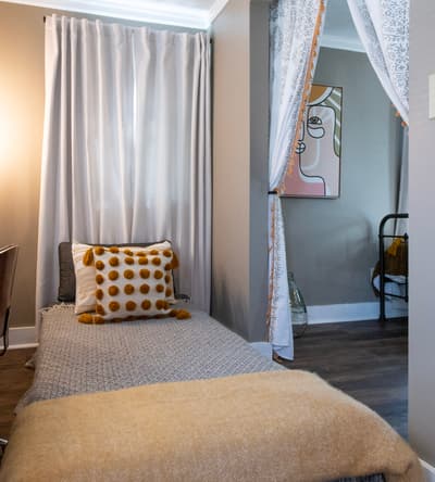 Sink into your cozy bed with soft textiles and warm tones, then peek behind the artistic curtain divider to discover your private bathroom retreat.