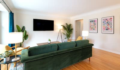 Unwind in your stylish living space with a plush emerald sofa, modern artwork, and tropical plants creating the perfect atmosphere for relaxation.
