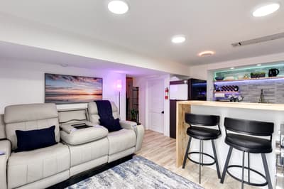 Unwind in your modern basement retreat with plush recliners, ambient lighting, and a sleek kitchen bar perfect for evening drinks.