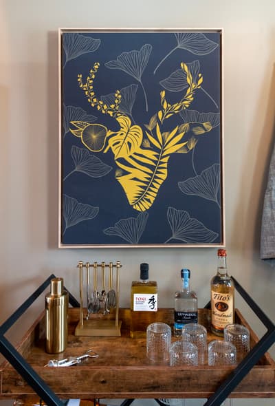Your stylish bar cart awaits with premium spirits and elegant glassware, perfectly positioned beneath striking botanical artwork for sophisticated evening cocktails.