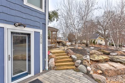 Blue shingle home with thoughtfully designed stone landscaping and wooden walkway, creating a welcoming neighborhood arrival experience.