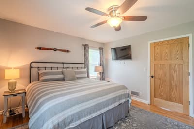 Unwind in your peaceful bedroom with cozy striped bedding, warm lighting, and a ceiling fan for perfect comfort.