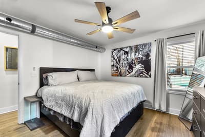 Drift off in this stylish bedroom with plush bedding, modern art, and a gentle ceiling fan keeping you cool.