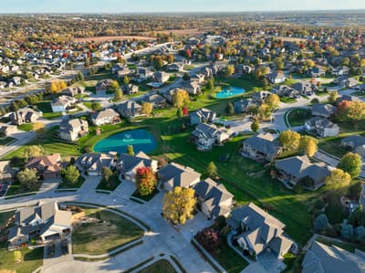 Aerial view of a well-established suburban neighborhood with mature trees, manicured lawns, swimming pools, and curving streets.