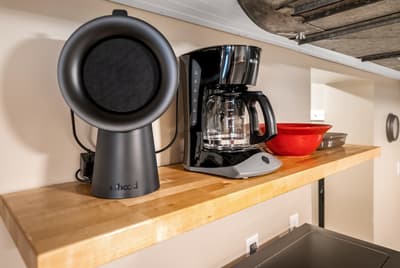 Your morning coffee awaits with modern appliances ready on warm wood shelving beneath rustic beams.