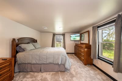 Your peaceful bedroom retreat features a plush bed and warm wood furnishings, with windows framing serene garden views for restful mornings.