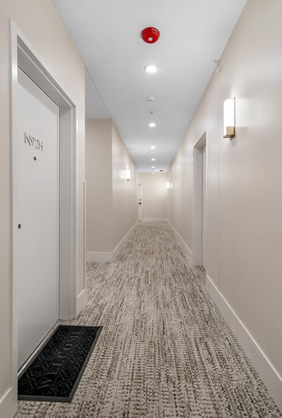Clean, well-lit hallway with modern carpet and lighting leads to your comfortable room.