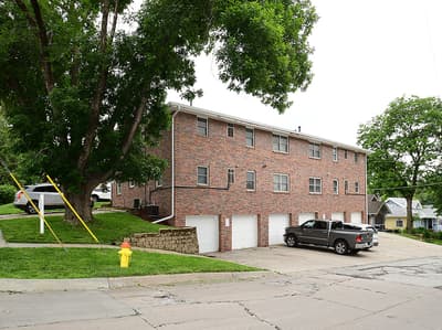 A two-story red brick building with multiple units and private garages, nestled on a quiet residential street lined with mature trees.