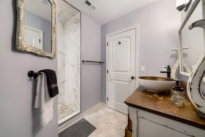 Step into your elegantly appointed bathroom featuring a stunning vessel sink on rich wood countertops and a luxurious marble-tiled shower.