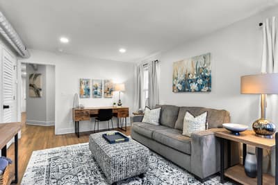 Relax in your stylish living space featuring a plush gray sofa, curated artwork, and warm lighting that creates the perfect ambiance for unwinding.