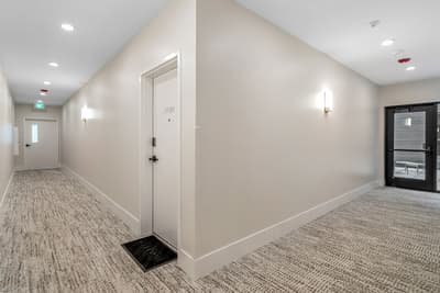 Clean, well-lit hallway leading to your private entrance with modern carpet and elegant wall sconces creating a welcoming arrival experience.