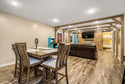 Your perfect entertainment basement with rustic beams, cozy seating, arcade fun, and sliding barn doors leading to peaceful sleeping quarters.