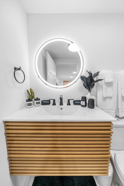 Freshen up in your stylish bathroom featuring a sleek illuminated mirror, warm wood vanity, and thoughtful touches that make mornings feel luxurious.