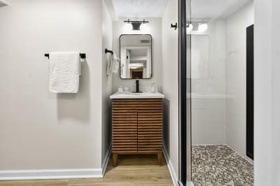 Step into your sleek bathroom featuring a walk-in shower with mosaic flooring and warm wood vanity.