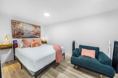 Unwind in your stylish sanctuary featuring a plush bed with cozy coral accents and a comfortable armchair perfect for morning coffee.